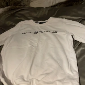 Vit långärmad tröja från Sail Racing - Säljer en stilren vit långärmad tröja från Sail Racing med svart logotyptryck på bröstet. Perfekt för en avslappnad och sportig look. Tröjan har en klassisk passform och är tillverkad i ett mjukt material.