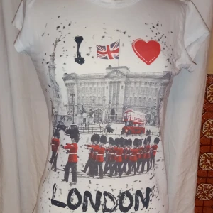 Vit t-shirt med London-motiv - Snygg vit t-shirt från NoS med ett coolt London-motiv. Trycket visar en klassisk scen med vakter, en dubbeldäckare och Union Jack-flaggan. Perfekt för dig som älskar London och vill ha en unik stil. Liten I storleken 