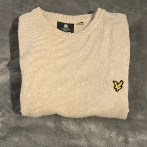 Beige stickad tröja från Lyle & Scott - Säljer en stilren beige stickad tröja från Lyle & Scott med deras ikoniska logga på bröstet. Tröjan har långa ärmar och en klassisk rund halsringning. Det ändå defekten är att tröjan är lite knopprig. Priset kan diskuteras!😄