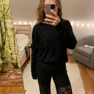 Svart tröja med volangdetalj från Bik Bok - Snygg svart tröja från Bik Bok med volangdetalj som går diagonalt över framsidan. Tröjan har långa ärmar och en rund halsringning, 