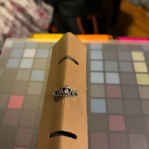 Silverfärgad ring med hjärtdetalj - Säljer en vacker silverfärgad ring med en hjärtdetalj i mitten och dekorativa mönster runtom. Perfekt för att ge en elegant touch till din stil.