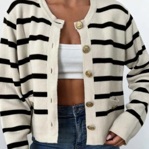 Randig kofta med guldknappar - Snygg randig kofta i beige och svart med dekorativa guldknappar. Koftan har långa ärmar och en croppad passform, perfekt för en stilren look.