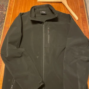 XDC jacka - Säljer en stilren svart jacka från XDC i storlek XL. Jackan har en dragkedja framtill och en praktisk ficka med dragkedja på ärmen. Perfekt för kyligare dagar.