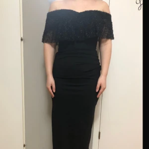 Svart offshoulder klänning - Elegant svart offshoulder klänning med glittriga detaljer och volang. Klänningen har en tight passform och är perfekt för festliga tillfällen.
