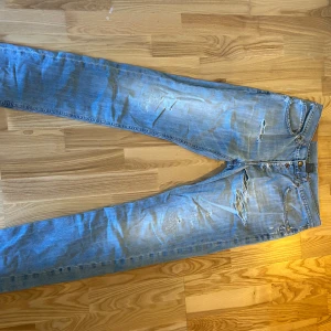 Dondup jeans - Säljer ett par blåa dondup jeans med coola slitningar och en klassisk femficksdesign. Jeansen har en dragkedja och knapp framtill. Perfekta för en avslappnad stil. Skicka gärna prisförslag!