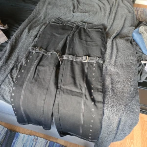 Svarta jeans med nitar och skärpdetaljer - Snygga svarta jeans, cargo stil med nitar och bältes detaljer. Vida ben, loose fit. Mått: längd 106 cm, midja 79 cm, höft 110 cm och lår 71 cm 
