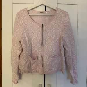 Rosa kofta RoseBud - Säljer en söt rosa kofta från RoseBud med ett diskret mönster och dragkedja framtill och två fickor🩷