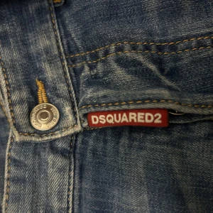 Blå jeans från DSQUARED2 - Snygga blå jeans från DSQUARED2 med slitna detaljer och en cool, distressed look. De har en klassisk femficksdesign och en knappgylf. Perfekta för en avslappnad stil med en touch av edge.