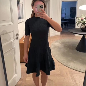 Mörkgrön ribbad klänning från Sandro - Snygg svart klänning från Sandro med ribbad överdel och korta ärmar. Kjolen har ett subtilt mönster och klänningen har en elegant passform som framhäver figuren. Perfekt för en stilren look.