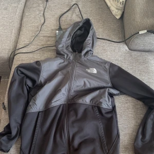Svart jacka från The North Face - Säljer en svart jacka från The North Face med huva och dragkedja. Jackan har en stilren design med långärmade ärmar och är perfekt för kyligare dagar.