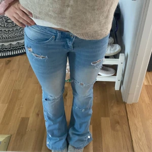 Lågmidjade jeans - Ljusblåa lågmidjade jeans med snygga detaljer som knappar och hål/slitningar. Väldigt bra skick! Storlek 36!!