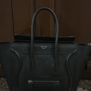 Svart handväska från Céline medium luggage bag - Elegant svart handväska från Céline i skinn med stilrena linjer och en praktisk dragkedja framtill. Väskan har två handtag och en rymlig insida, perfekt för att bära med sig det nödvändigaste. En tidlös accessoar för den stilmedvetna.