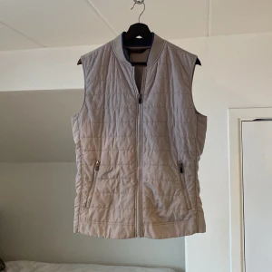 Grå väst från Zara - Grå quiltad väst från Zara med dragkedja framtill. Perfekt för lager-på-lager under kyligare dagar. Västen har en stilren design med ribbad krage och praktiska fickor med dragkedja. Storlek L väldigt liten i storlek, passar S-M