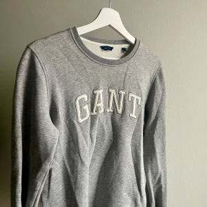 Grå sweatshirt från GANT - Säljer en stilren grå sweatshirt från GANT med deras logga i vitt på bröstet. Tröjan har rund hals och långa ärmar, perfekt för en avslappnad look. Passar bra till tex jeans. Använd ytterst få gånger!