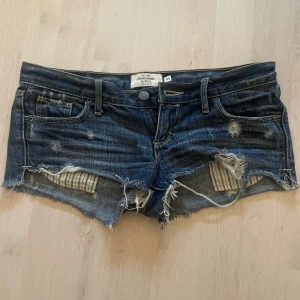 Blå jeansshorts från Abercrombie & Fitch - Säljer ett par snygga blå jeansshorts från Abercrombie & Fitch. De har en sliten look med fransiga kanter och slitningar fram och bak. Perfekta till sommaren!! Obs dragkedjan hoppar ur ibland men även om den inte går att få igen så är det inget som syns när byxorna är på❤️❤️