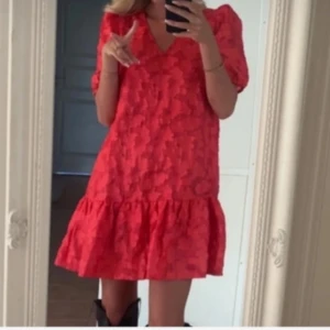 Röd/rosa klänning med volang - Trendig röd klänning med volangdetalj och korta ärmar. Perfekt för en färgglad look. Den har en lös passform och ett subtilt mönster som ger extra stil.