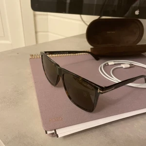 Tom Ford fletcher - Snygga solglasögon från Tom Ford med en klassisk design. Bågarna är i en mörkbrun nyans med en subtil leopardmönster. Glasen är mörka och ger ett stilrent intryck. Perfekta för soliga dagar!