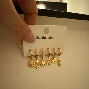 Guldpläterades örhängen i rostfritt stål - Set med sex guldpläterade örhängen i rostfritt stål. Varje örhänge har en unik charm: fyrklöver, fisk, hjärta, katt, teddy och fiskben. Perfekt för att mixa och matcha efter humör och stil.