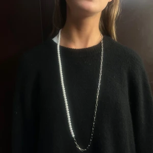 013 - Elegant långt halsband med vita pärlor. Perfekt för att ge en klassisk touch till din outfit. Halsbandet har en enkel och stilren design som passar till många olika stilar.