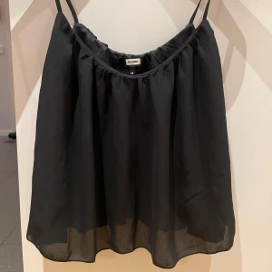 Svart ärmlös topp från Bik Bok - Säljer en stilren svart ärmlös topp från Bik Bok i storlek M. Toppen har tunna axelband och en luftig passform, perfekt för varma dagar. Enkel och elegant design som passar till många olika outfits.
