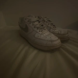 Vita Nike Air Force sneakers - Säljer ett par klassiska vita och gråa Nike Air Force sneakers. Skorna har en ikonisk design med snörning och Nike-logga på sidan. Perfekta för en stilren look.