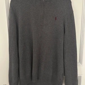 Grå sweatshirt quarter zip, Ralph Lauren - Säljer en stilren grå tröja från Ralph Lauren med halv dragkedja och broderad Ralph Lauren logotyp på bröstet. Tröjan är stickad och har ribbade detaljer vid krage och ärmslut. Mycket bra skick. Storlek L men skulle säga att den sitter mer som en M.