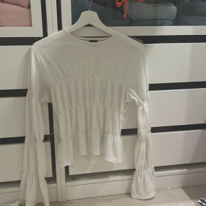 Vit blus från Gina Tricot - Säljer en stilren vit blus från Gina Tricot i storlek XS. Blusen har långa ärmar och volangdetaljer som ger en trendig look. Perfekt för att lyfta din outfit med en touch av elegans.