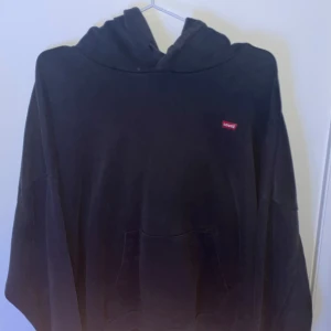 Levi's hoodie svart - Säljer en svart hoodie från Levi's med klassisk design och röd logga på bröstet. Tröjan har en rymlig passform och en praktisk känguruficka framtill. Perfekt för en avslappnad stil.