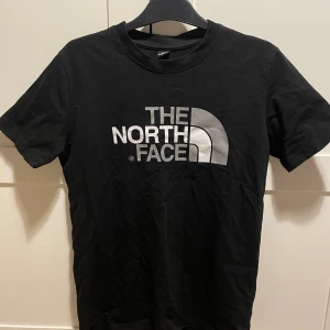 Svart t-shirt från The North Face - Snygg svart t-shirt från The North Face med deras ikoniska logga i vitt på både framsidan och baksidan. Perfekt för en casual look. Tillverkad i mjukt material för extra komfort.