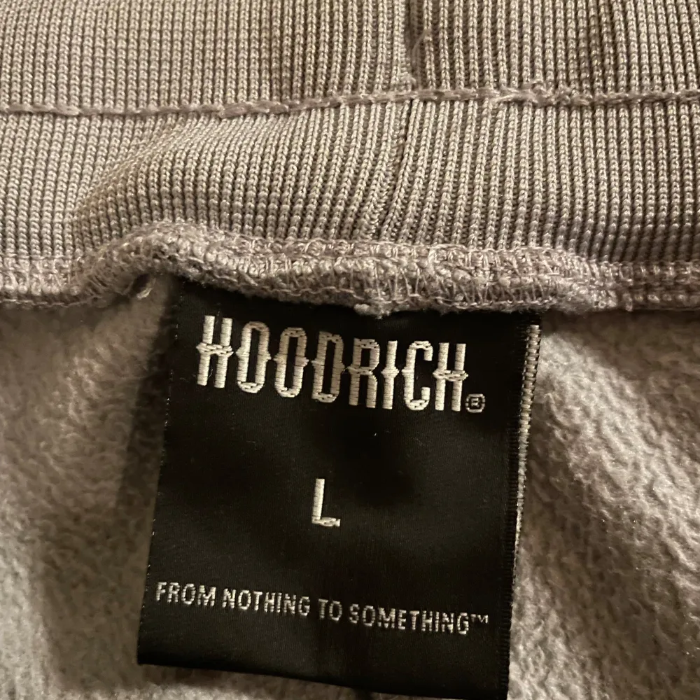 Säljer ett par grå mjukisbyxor från Hoodrich i storlek L. Byxorna har en bekväm passform med elastisk midja och dragsko. De har en cool design med texten 'Hoodrich Lifestyle Worldwide Organisation' tryckt på benet och en praktisk dragkedjeficka. Perfekta för en avslappnad stil!. Jeans & Byxor.