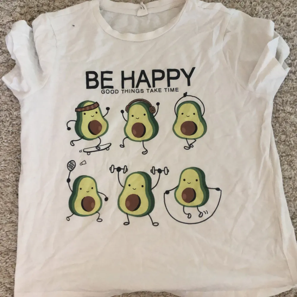 Säljer en söt vit t-shirt från Shein med ett roligt avokadotryck och texten 'Be Happy, Good Things Take Time'. T-shirten är kortärmad och gjord av bomull, perfekt för en avslappnad och glad stil. Den är i bra skick men fortfarande supercharmig!. T-shirts.