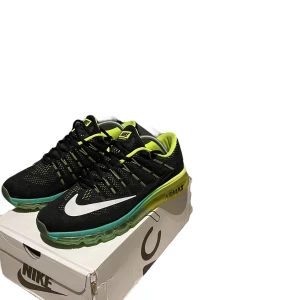 Svarta Nike Air Max sneakers med gröna detaljer - Säljer ett par svarta Nike Air Max sneakers med gröna detaljer. Skorna har en snygg design med en vit Nike-logga på sidan och en genomskinlig sula som ger en cool effekt. De är i nyskick och perfekta för både träning och vardagsbruk. 