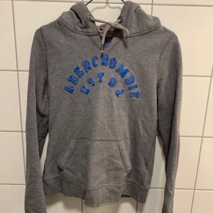 Grå hoodie från Abercrombie & Fitch  - Grå hoodie med blå glittertext, sitter som den ska men sitter ganska tajt på mig och jag har storlek XS-S, storlek S, finns vissa tecken på användning som syns på bilderna