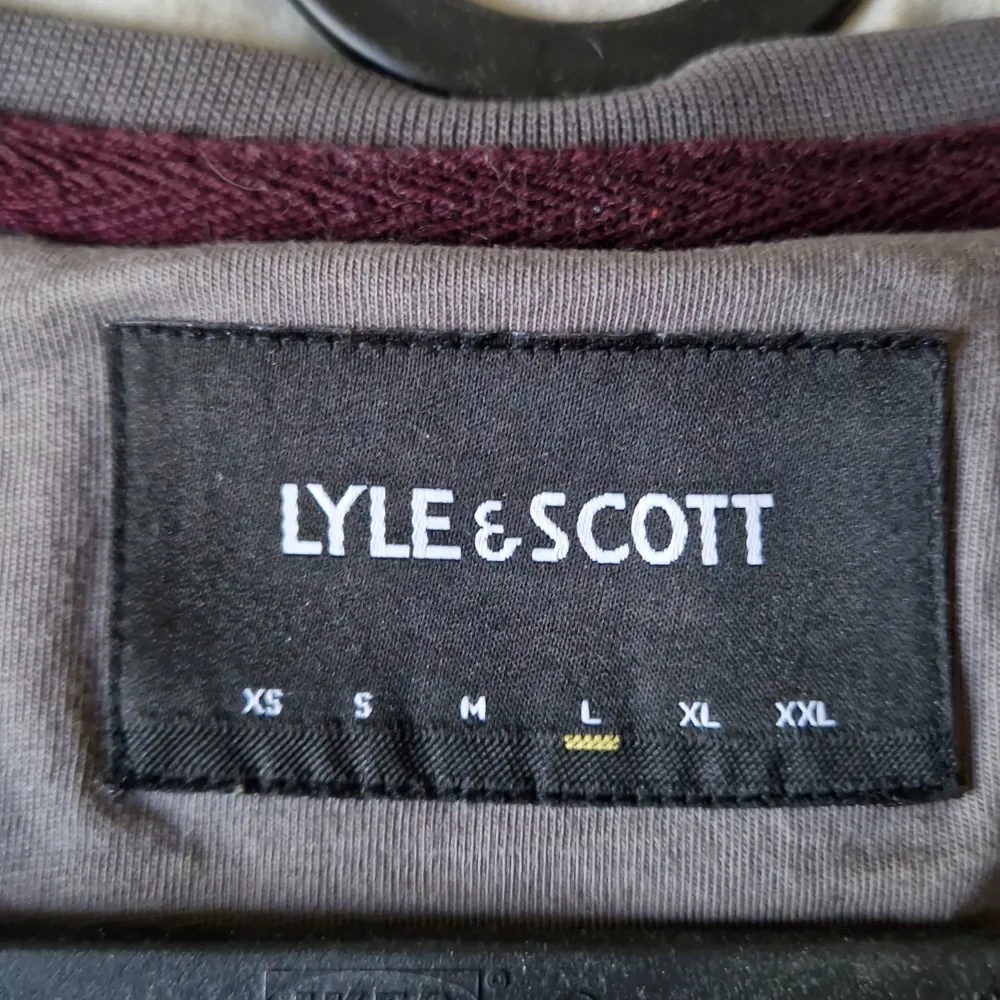 Säljer en snygg grå t-shirt från Lyle & Scott i storlek L. Den har en cool vinröd bröstficka med en broderad gul logga. T-shirten är kortärmad och gjord av 100% bomull, vilket gör den superbekväm. Perfekt för vardagsbruk eller en avslappnad dag ute!. T-shirts.