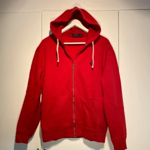 Polo Ralph Lauren Zip-Hoodie  - Polo Ralph Lauren Zip-Hoodie i röd färg med marinblå häst. Välanvänd men inga skador. Nypris 1900kr. Produceras ej längre. Enormt bra plagg att kunna dressa upp & ner, stilsäker & ikonisk. Storlek M. Pris kan diskuteras. Hörs i DM! 