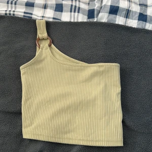 Beige ribbad oneshoulder topp - Säljer en superfin olivgrön ribbad topp med oneshoulder-design. Den har en cool ringdetalj på axelbandet som ger en extra touch. Perfekt för sommardagar eller en utekväll!