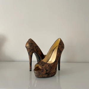 Oanvända NELLY klackar - Helt oanvända Nelly klackar med ormmönster i svart och roséguld. Klackarna är mer skimriga och holografiska i verkligheten. Modellen går ej att få tag på längre. Inga täcken på användning och helt ren sula. Klacken är 14 cm hög❤️