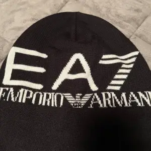 Säljer en snygg svart mössa från Emporio Armani med vit logga. Den är perfekt för att hålla dig varm och stilren under kalla dagar. Mössan är i ett mjukt och bekvämt material.köpt 2år sen typ använd typ 3-4gånger, slutsåld överallt!