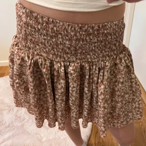 Blommig kjol med volang - Säljer en superfin blommig kjol med volangdetaljer. Den har en elastisk midja som gör den bekväm och lätt att bära. Perfekt för sommardagar eller en avslappnad vårutflykt. Kjolen är i ett mjukt och luftigt material, vilket gör den idealisk för varmare väder.