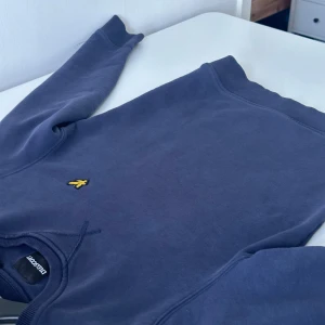 Mörkblå tröja från Lyle & Scott storlek XXs - Säljer en stilren mörkblå tröja från Lyle & Scott med deras ikoniska logga på bröstet. Tröjan har långa ärmar och en rund halsringning, perfekt för en avslappnad look.