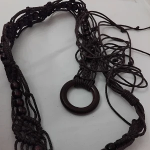 Brunt flätat bälte med trädetaljer - Skärp, mörkbrunt, makrame med träkulor. Enbart makramen är 75 cm, träringen ca 5,5 cm och snörena ca 45 cm. Oanvänt. Swish vid upphämtande, finns i centrala Kalix.