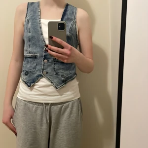 Jeansväst med knappar - Snygg jeansväst med knappar framtill och två fickor. Perfekt för en avslappnad stil. Västen har en klassisk blå jeansfärg och är ärmlös.