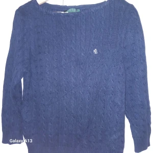 Mörkblå stickad tröja från Ralph Lauren - Säljer en snygg mörkblå stickad tröja från Ralph Lauren med kabelstickat mönster. Tröjan har långa ärmar och en liten logotyp på bröstet. Perfekt för kyliga dagar!