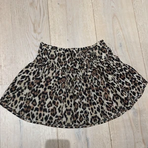 Leopardmönstrad kjol från Gina Tricot - Snygg leopardmönstrad kortkjol från Gina Tricot. Kjolen har en volangdetalj och är perfekt för att ge en trendig touch till din outfit. Den är gjord i ett lätt och bekvämt material som passar bra för varmare dagar.