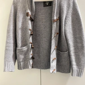 Grå stickad kofta med träknappar - Säljer en mysig grå stickad kofta med unika träknappar och två praktiska fickor framtill. Perfekt för kyliga dagar och ger en stilren look. Koftan har långa ärmar och ribbade kanter för extra komfort passar dig som är mellan 150-160|| Hör av dig vid minsta fundering!! Priset går att diskutera 