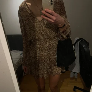 Mönstrad klänning med volangdetaljer - snygg mönstrad klänning  med volangdetaljer. Klänningen har en v-ringad hals och långa ärmar, perfekt för både vardag och fest. Den har en smickrande passform med resår i midjan som ger en fin siluett❣️