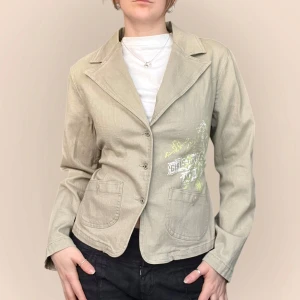 Beige kavaj med tryck - Snygg  2000s kavaj med  tryck i vitt och grönt på framsidan. Har ett bälte som kan dra åt midjan och är även lite stretchig! Jag på bilden har strl 36 på överdelar och är 170cm. Klicka på köp nu <3