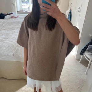 Beige stickad poncho  - Säljer en stilren beige poncho med hög krage. Perfekt för lager-på-lager och ger en avslappnad look. Passar bra till både kjol och byxor. Ett mångsidigt plagg för alla säsonger.