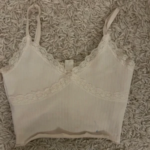 Beige ribbad linnetopp med spetsdetaljer - Säljer en söt beige ribbad linnetopp med smala axelband och spetsdetaljer längs kanterna. Perfekt för varma dagar eller som ett lager under en tröja. Toppen har en mjuk och bekväm passform. Fraktar endast varan och köparen betalar frakten! Priset som syns är det som gäller🫶🙏