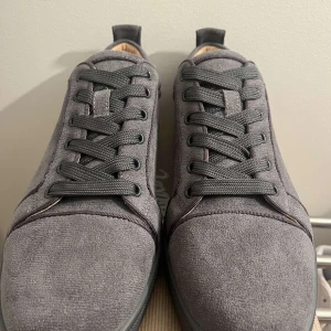 Grå sneakers från Christian Louboutin - Snygga grå sneakers i mocka från Christian Louboutin med den ikoniska röda sulan. Skorna har snörning och en stilren design som passar perfekt för en trendig look.